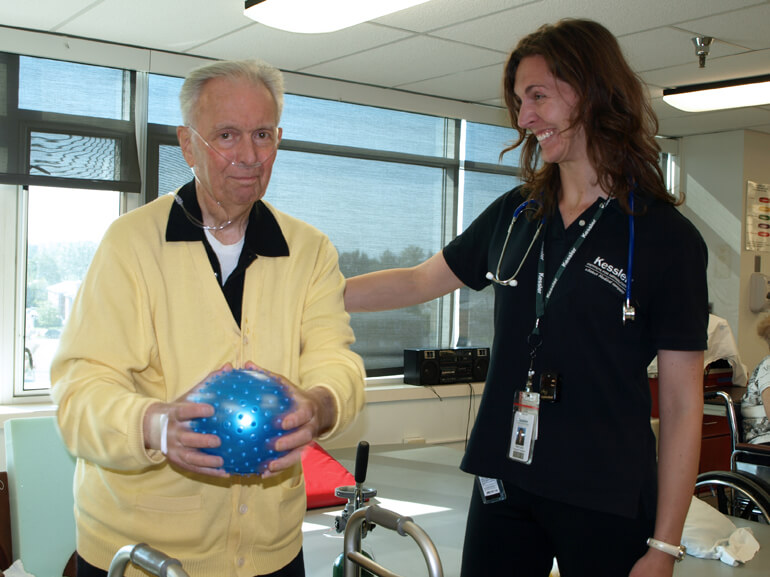 Senior male patient with walker working with therapist using a small rubber therapy ball