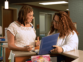 Two women looking at financial records at nurse's station in a hospital.