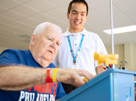 A male patient with white hair placing yellow blocks in a small blue container.