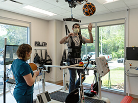 Young male patient in overhead safety harness walking on a treadmill in a therapy gym.