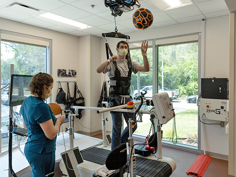 Young male patient in overhead safety harness using a treadmill in a therapy gym.