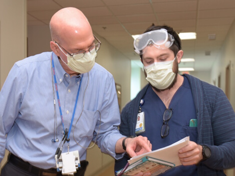 Male doctor and male therapist in hospital hallway reviewing a patient chart.