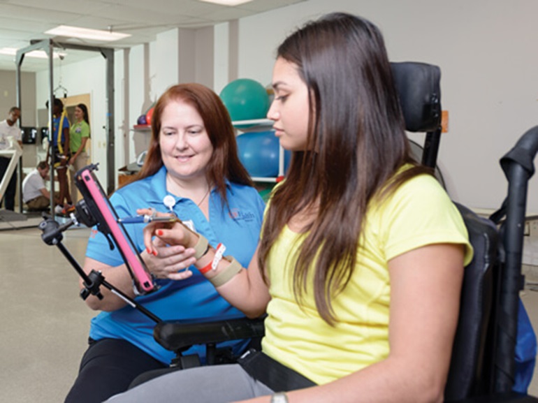 Female therapist sitting next to young female patient using an electronic pen to write on a tablet computer.