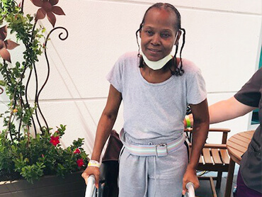 Deloris standing with the help of a walker in an outside cafe.