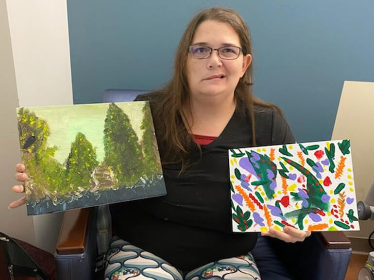 Tasha holding two of her art therapy paintings.