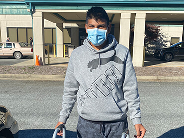 Christian wearing a blue hospital mask and standing outside the hospital with a walker.