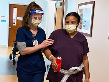 A female therapist assisting Purette in walking a hospital hallway.